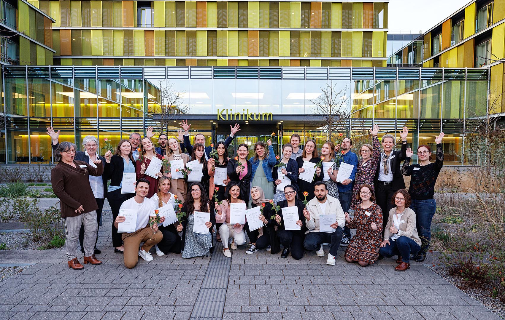 Die 17 neuen Pflegefachfrauen und -männer sowie ihre Ausbilder mit Zeugnis und Blumen vor dem Klinikum Winnenden